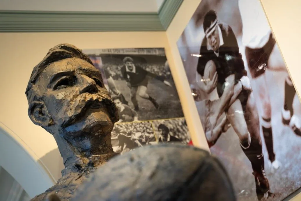 A bust sculpture of a former athlete sits in the Sports Hall of Fame with a rugby photograph in the background.