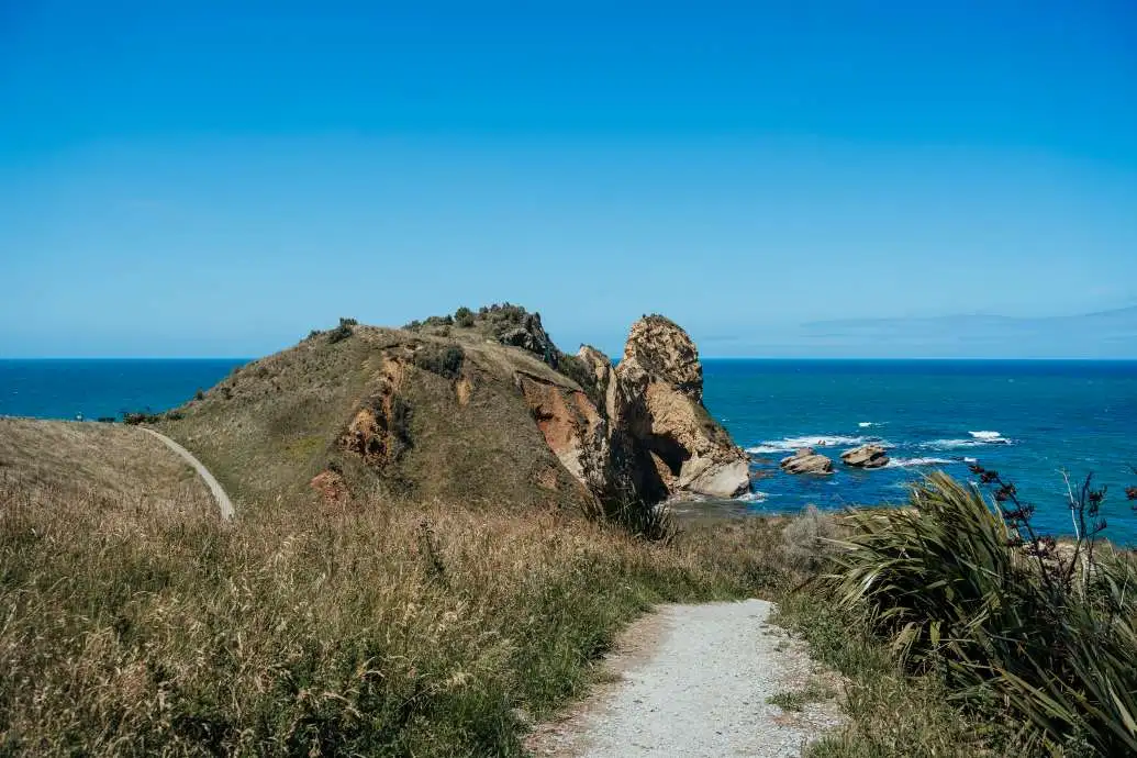 The Huriawa Peninsula stretches out towards the ocean on a blue sky day.