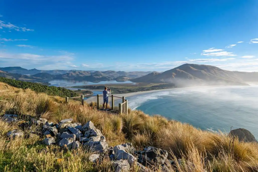 A man takes a photo of a stunning vista from a lookout on a sunny day.