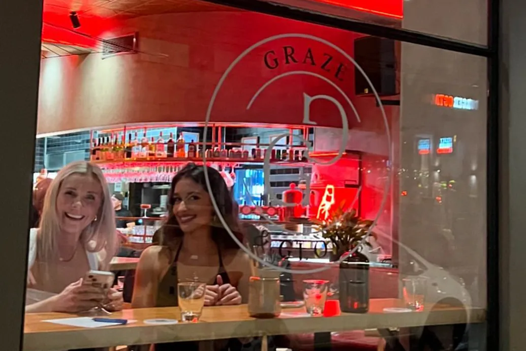 Two women smiling as they wait for a table at Graze and Glow. 