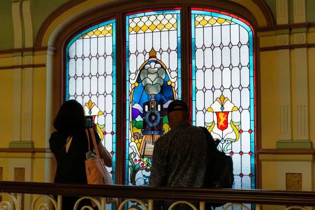 Two visitors examine the stained-glass window of a locomotive at the Dunedin Railway Station.