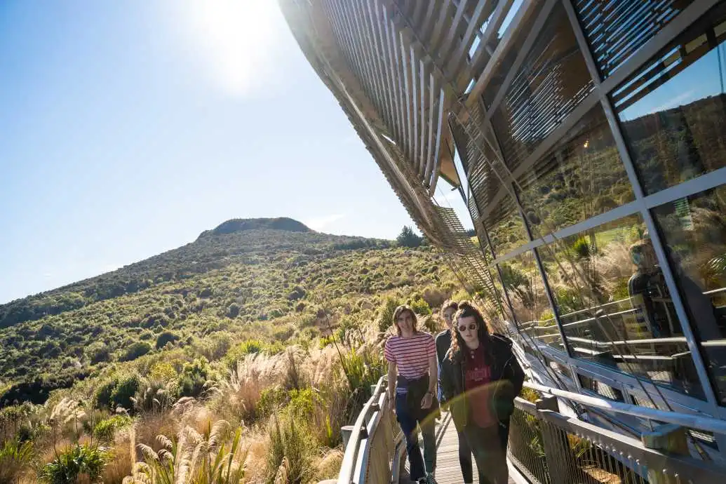 A group of young tourists walk around the edge of the Orokonui Ecosanctuary centre with hinterland in the background.