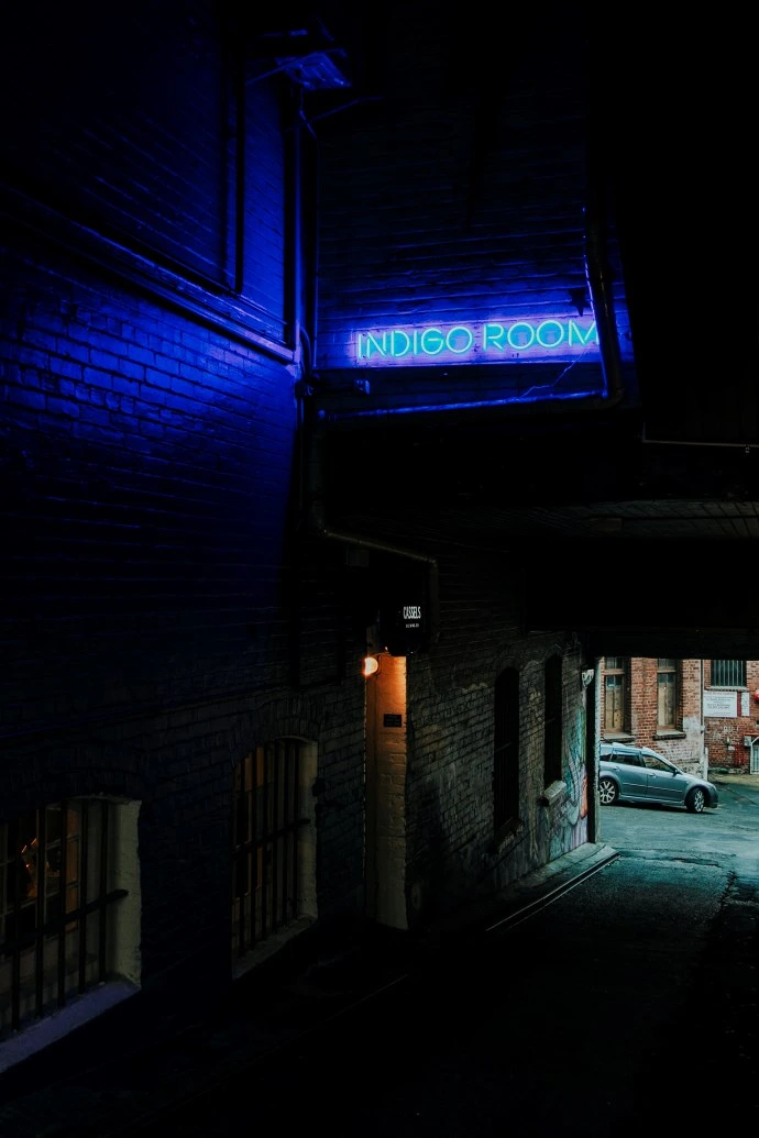 Indigo Room alley A neon blue light saying Indigo Room shines on a street art-adorned alley.