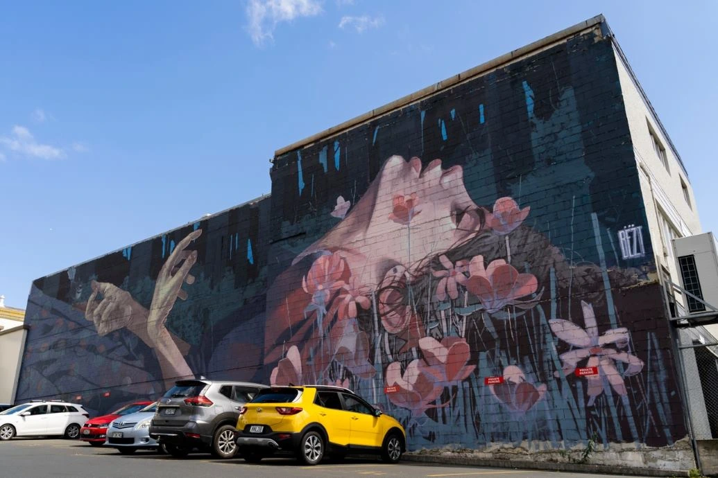 Street Art Trail Bezt A mural in a carpark depicts a woman dying in a field of flowers.