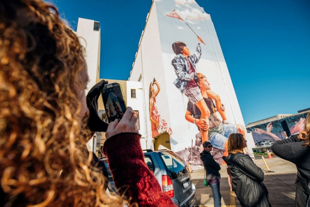 Street Art Trail Fintan Magee People take photos of a large mural depicting children catching clouds with a butterfly net.