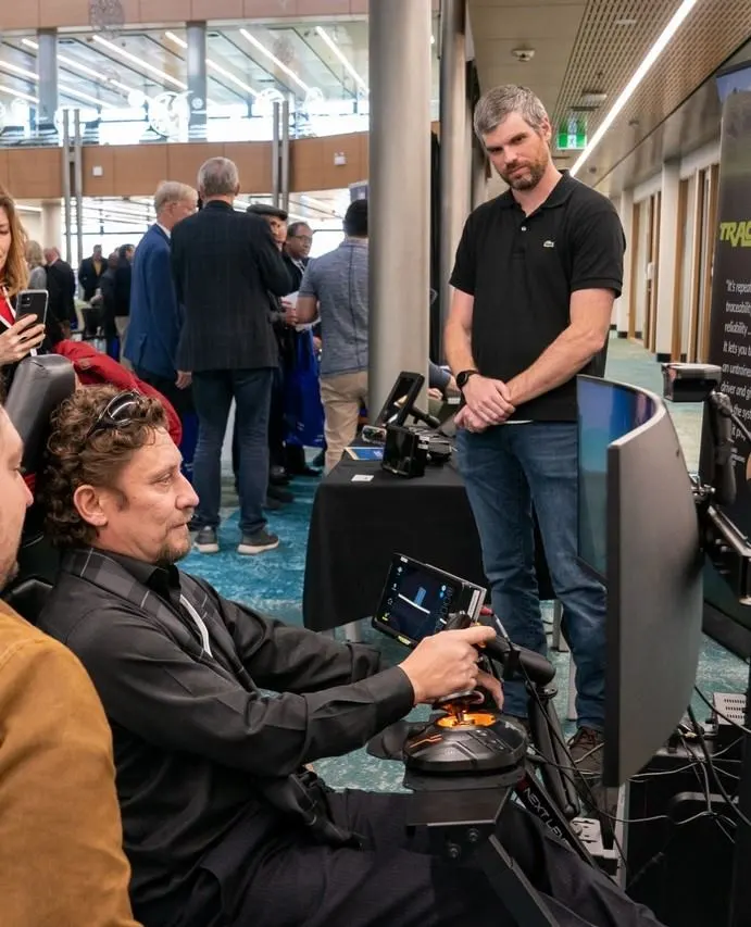 A small group at a conference observes a man testing out the hardware of a local tech business.