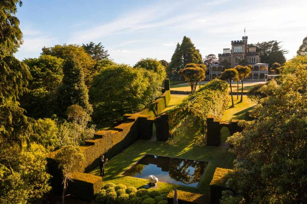 Larnach Castle is seen in the background with the sloping green garden in the foreground.